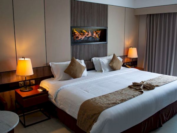 A hotel room with a neatly made bed, pillows, bedside tables with lamps, curtains, and a decorative wall piece above the bed.