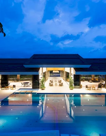 A luxurious modern hotel or resort with a large illuminated pool at night, surrounded by palm trees and elegant architecture.