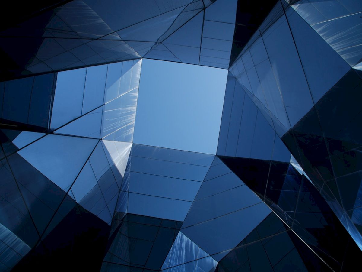 The image shows a geometric pattern of mirrored glass panels forming an abstract architectural design with a central view of the sky.