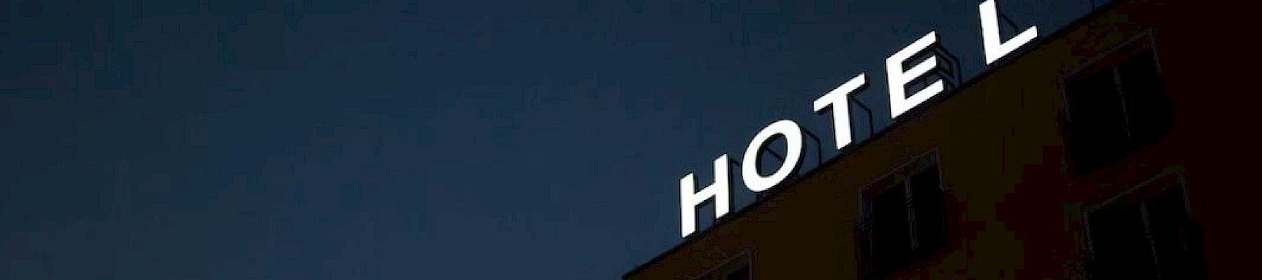 The image shows a building with the illuminated sign "HOTEL" against a dark sky at dusk or night, suggesting accommodation.