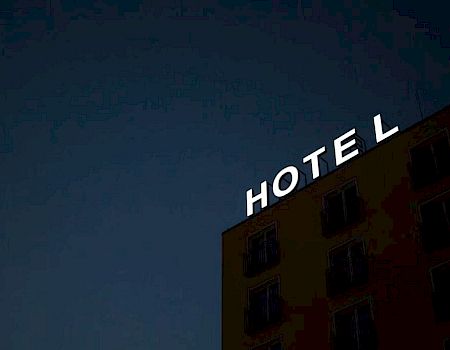 The image shows a building with the illuminated sign "HOTEL" against a dark sky at dusk or night, suggesting accommodation.