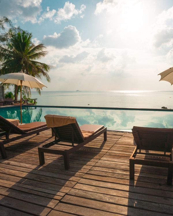 A serene beach scene with lounge chairs, umbrellas, and palm trees overlooking a tranquil ocean under a bright sky with fluffy clouds.