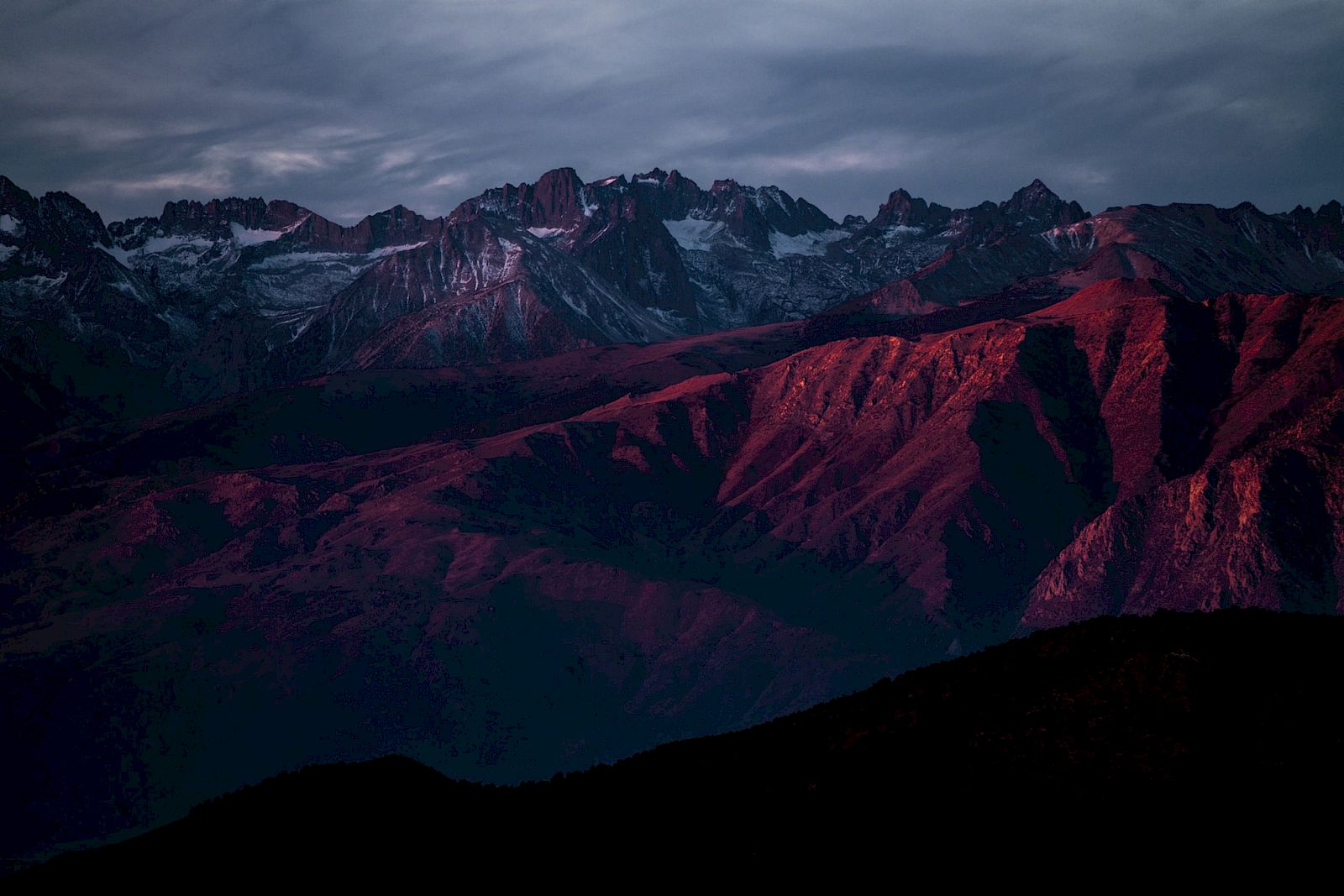 A mountain range with a purplish-red hue under a cloudy sky during twilight.