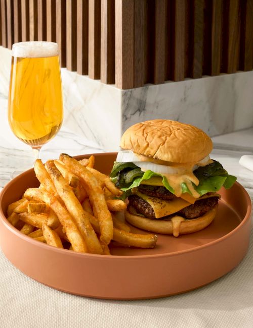 A cheeseburger with lettuce, fries, and a glass of beer on a table.