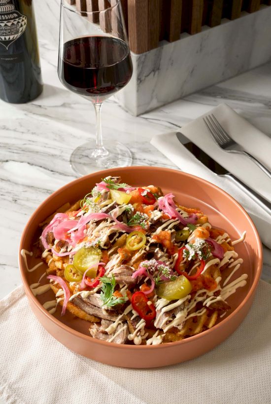 The image shows a dish with a variety of toppings alongside a glass of red wine. There are also utensils and a napkin on the table.