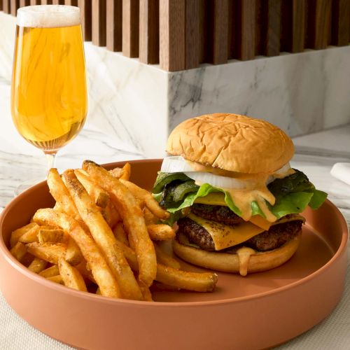 A cheeseburger with lettuce is served with fries on a plate, accompanied by a glass of beer on the side.