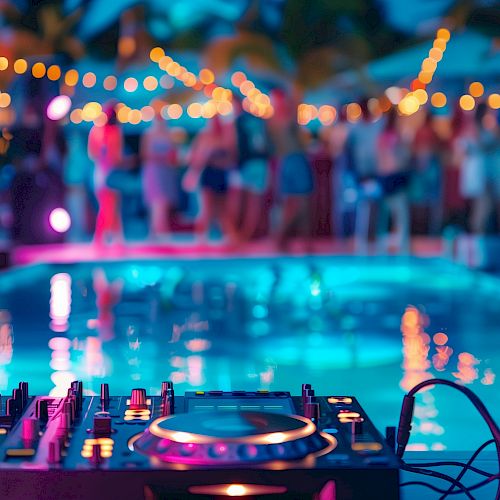 A DJ setup by a pool with blurred people and string lights in the background, creating a party atmosphere.