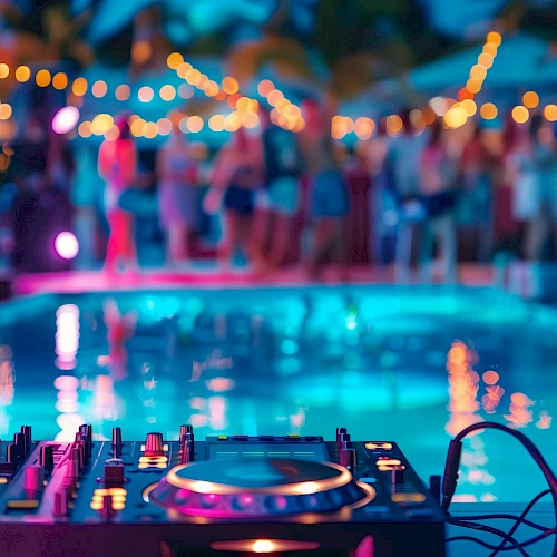 A DJ setup by a pool with blurred people and string lights in the background, creating a party atmosphere.