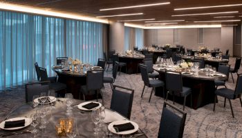 The image shows an elegantly set dining room with round tables, black chairs, and dim lighting, ready for an event or banquet.