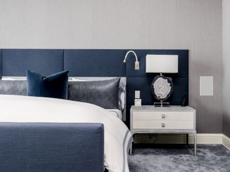 A modern bedroom with a blue headboard, white bedding, nightstand, lamp, and decorative items.