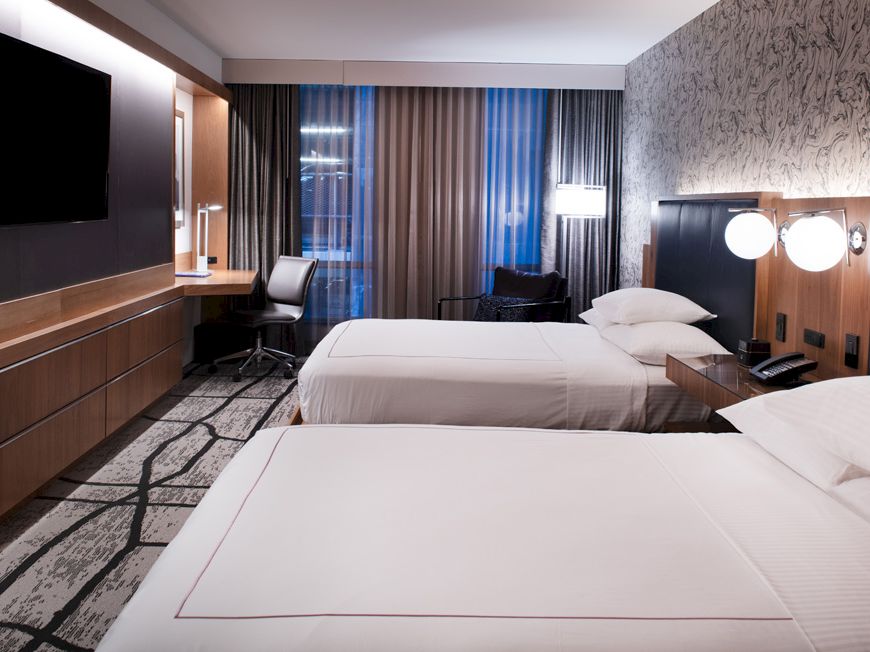 A modern hotel room with two beds, a large TV, desk area, and stylish lighting.