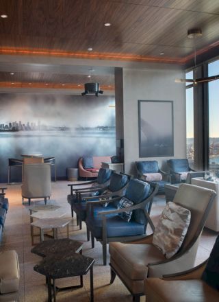 A stylish lounge with modern seating, large windows, and a view of water, featuring a cityscape wall mural for a cozy atmosphere.