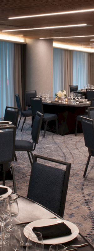 The image shows an elegantly set banquet hall with round tables, black chairs, and decorative place settings, all under warm lighting.