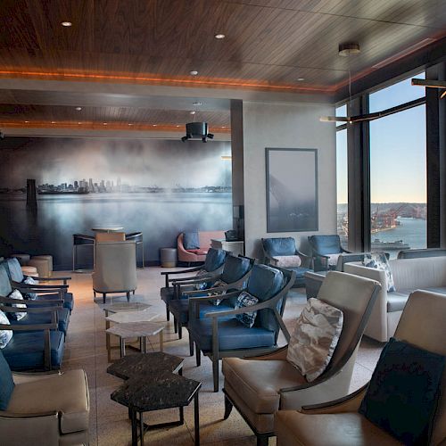 A modern lounge with rows of chairs, a large wall mural, and windows offering a scenic view of water and hills.
