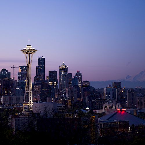The image shows the Seattle skyline at dusk, with the Space Needle prominently visible, and Mount Rainier in the background.