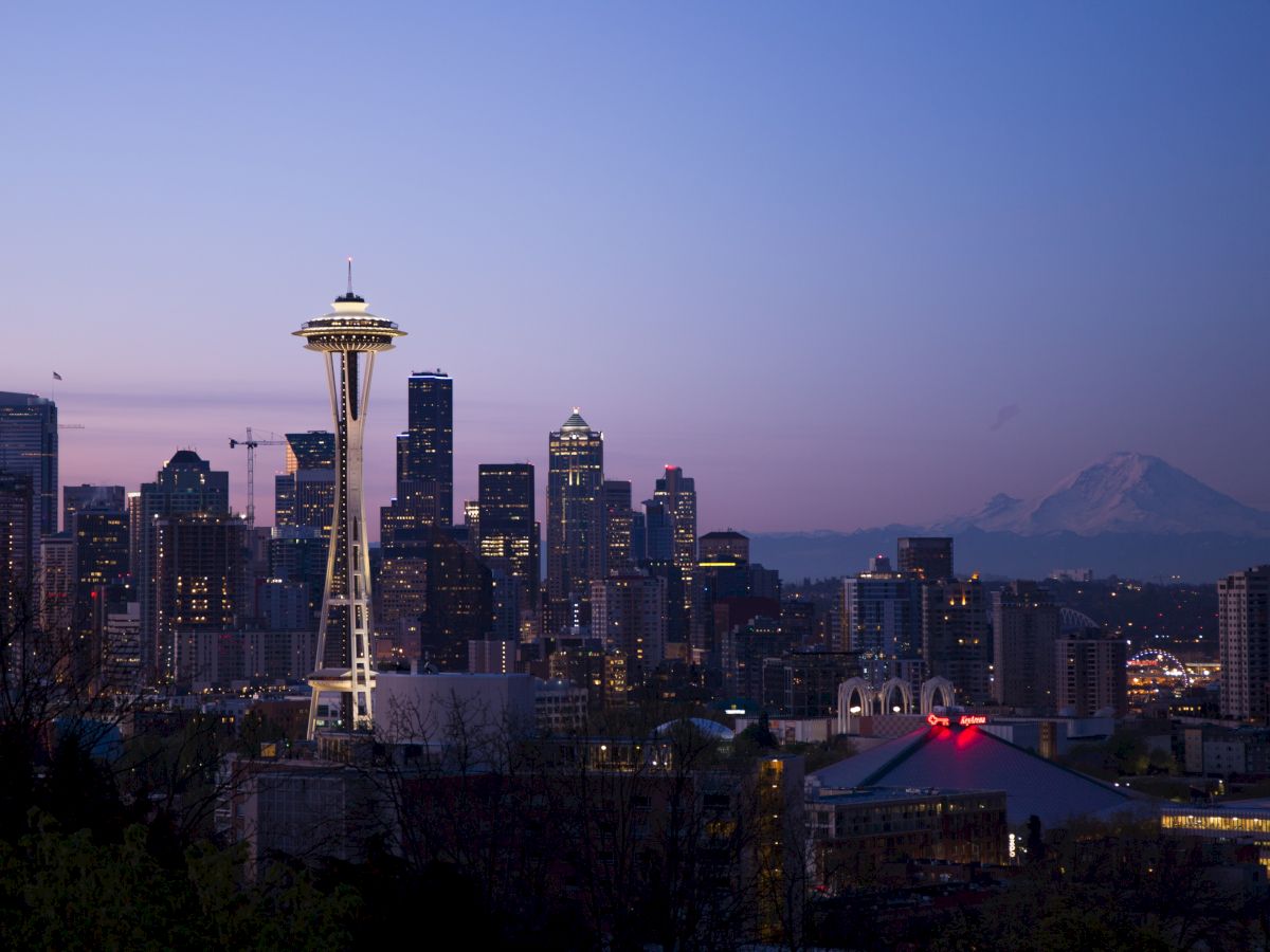 The image shows the Seattle skyline at dusk, featuring the Space Needle and Mount Rainier in the background under a purple sky.