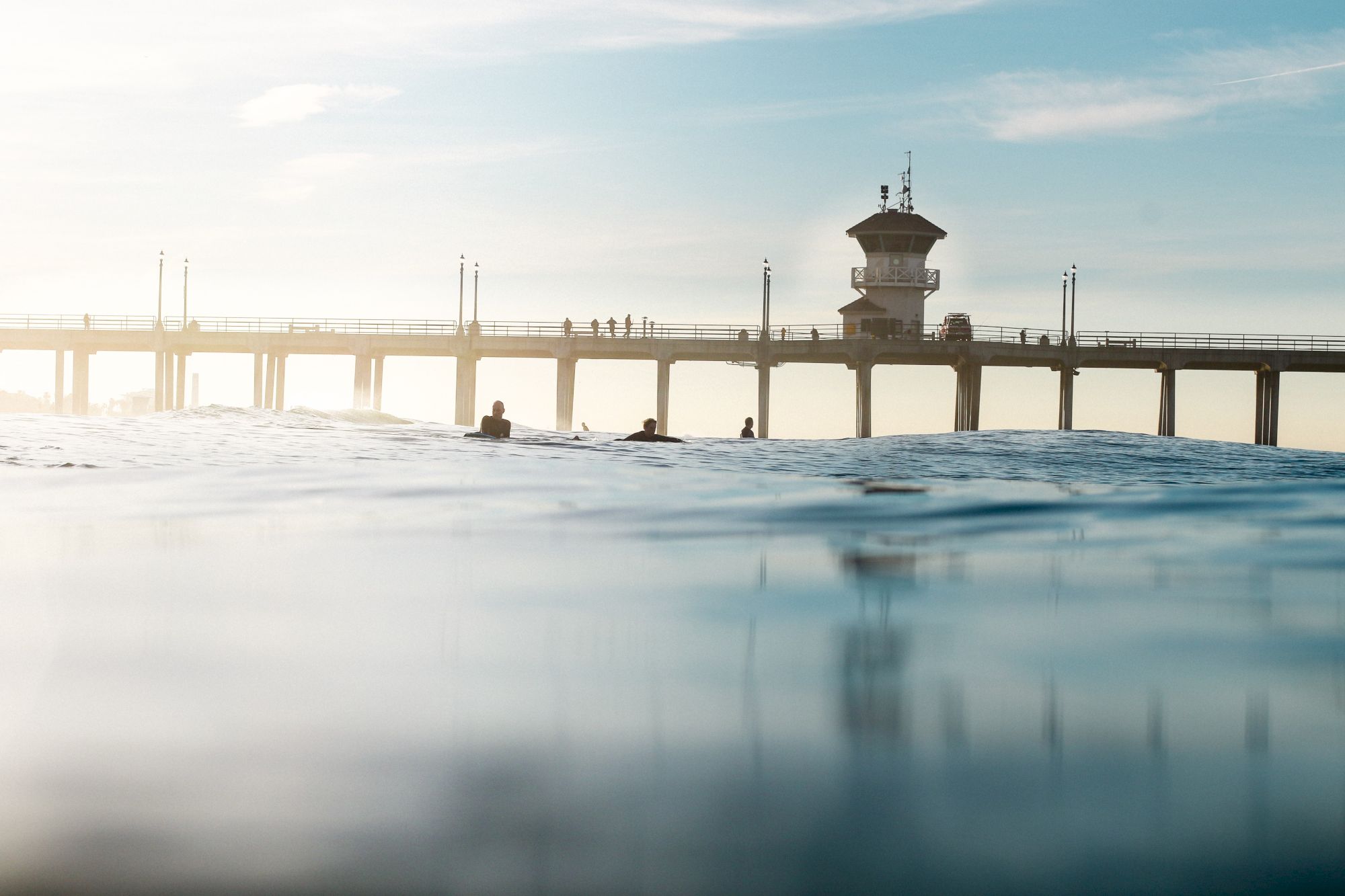 The image shows a serene ocean view with a pier extending across the water, silhouetted by a bright sky, creating a peaceful scene.